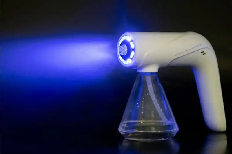 Weiße, handgehaltene Desinfektionspistole mit einem transparenten Wassertank, die einen feinen Sprühnebel unter blauem LED-Licht vor einem dunklen Hintergrund ausstößt