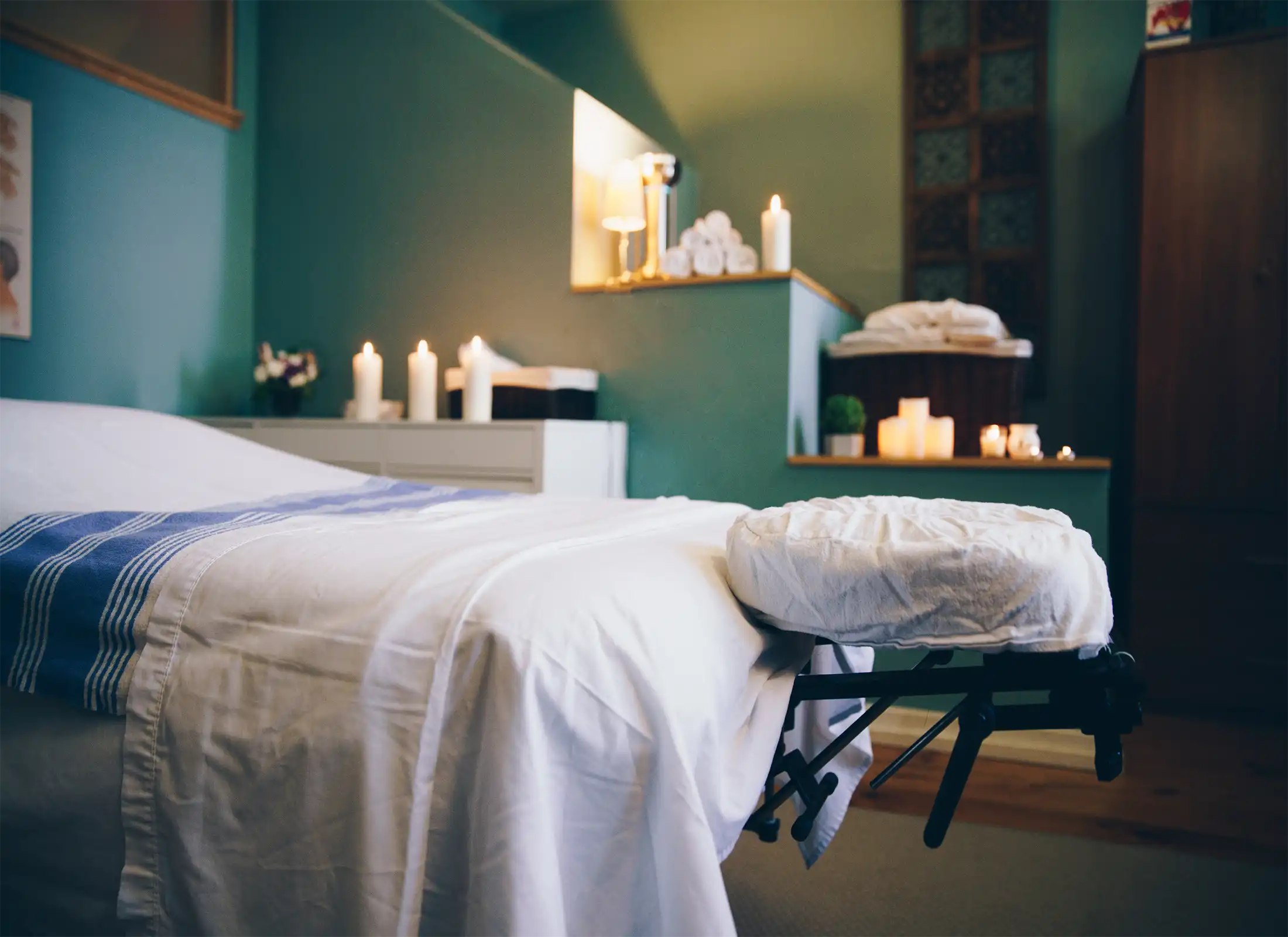 Massageliege in einem ruhigen Wellnessbereich mit Kerzenschein.